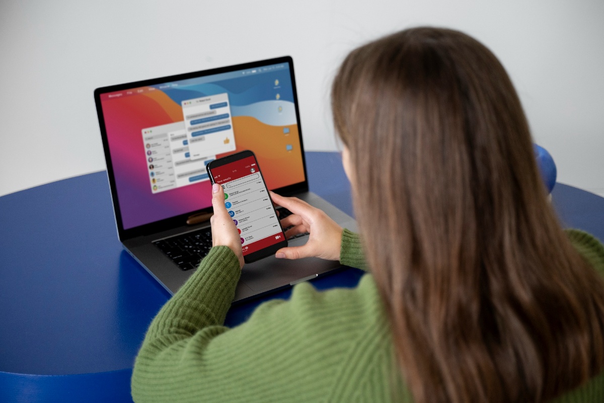 Mulher mexe no celular em frente a um laptop